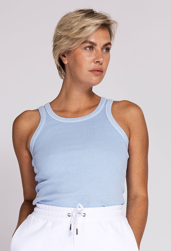 Woman wearing a light blue tank top and white pants against a plain background